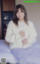 A woman sitting on top of a bed wearing a white sweater.