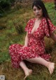 A woman in a red dress sitting in the grass.