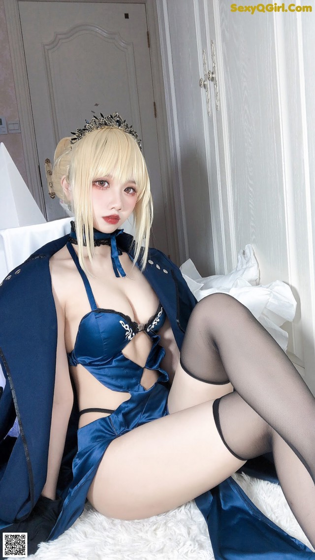 A woman in a blue dress and black stockings sitting on a bed.