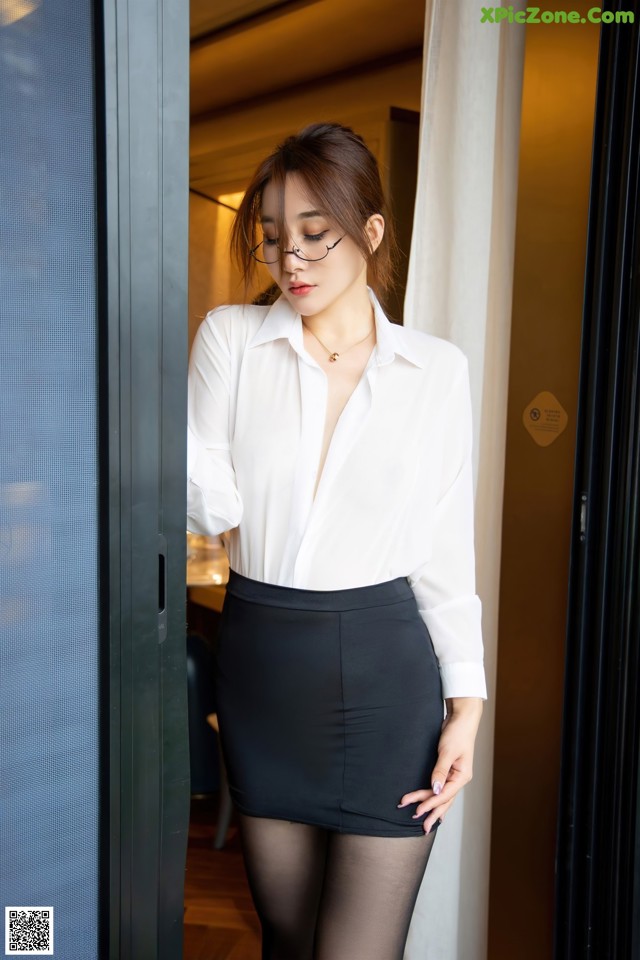 A woman in a white shirt and black skirt posing for a picture.