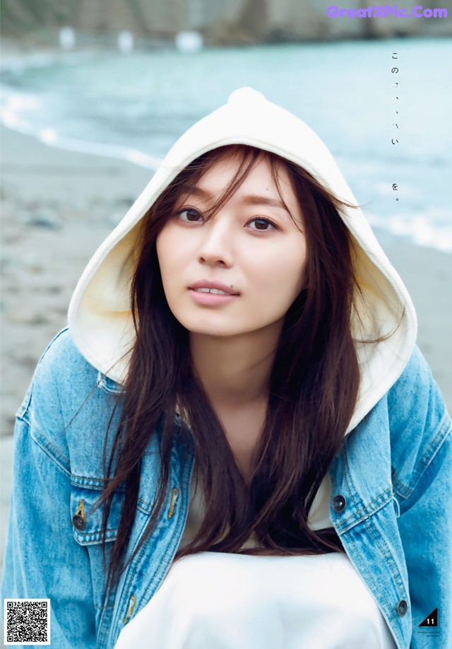 A woman wearing a white hoodie sitting on a beach.
